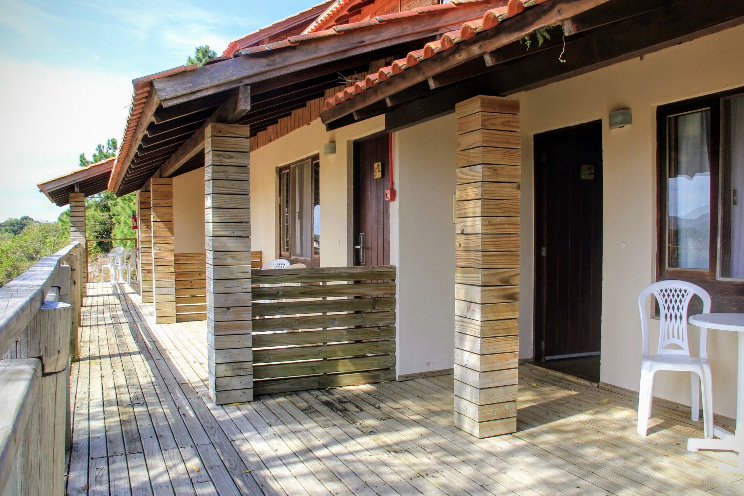 Una terraza de madera con una zona techada, una silla de plástico blanca y una puerta.