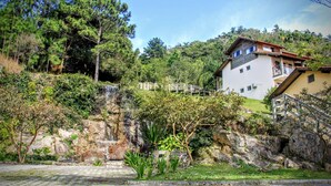 Un bâtiment à deux étages doté d’un balcon, entouré d’une végétation luxuriante et agrémenté d’une petite cascade.