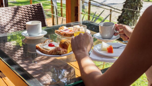 Une terrasse en bois avec une table en verre, mise pour le petit-déjeuner.