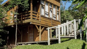 Une cabane en bois dotée d’un balcon, entourée d’herbe et d’arbres.