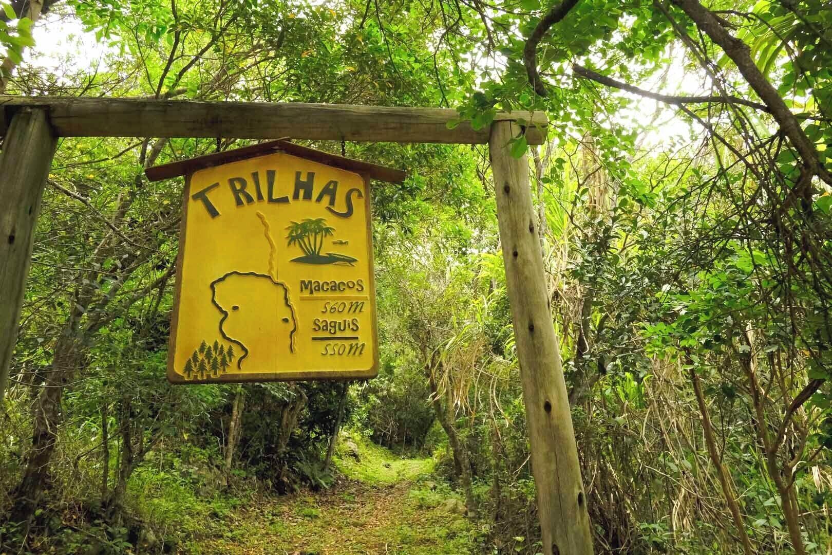 Ein gelbes Schild mit der Aufschrift 'TRILHAS' und der Silhouette einer Person, das einen Bereich für Übernachtungen kennzeichnet.