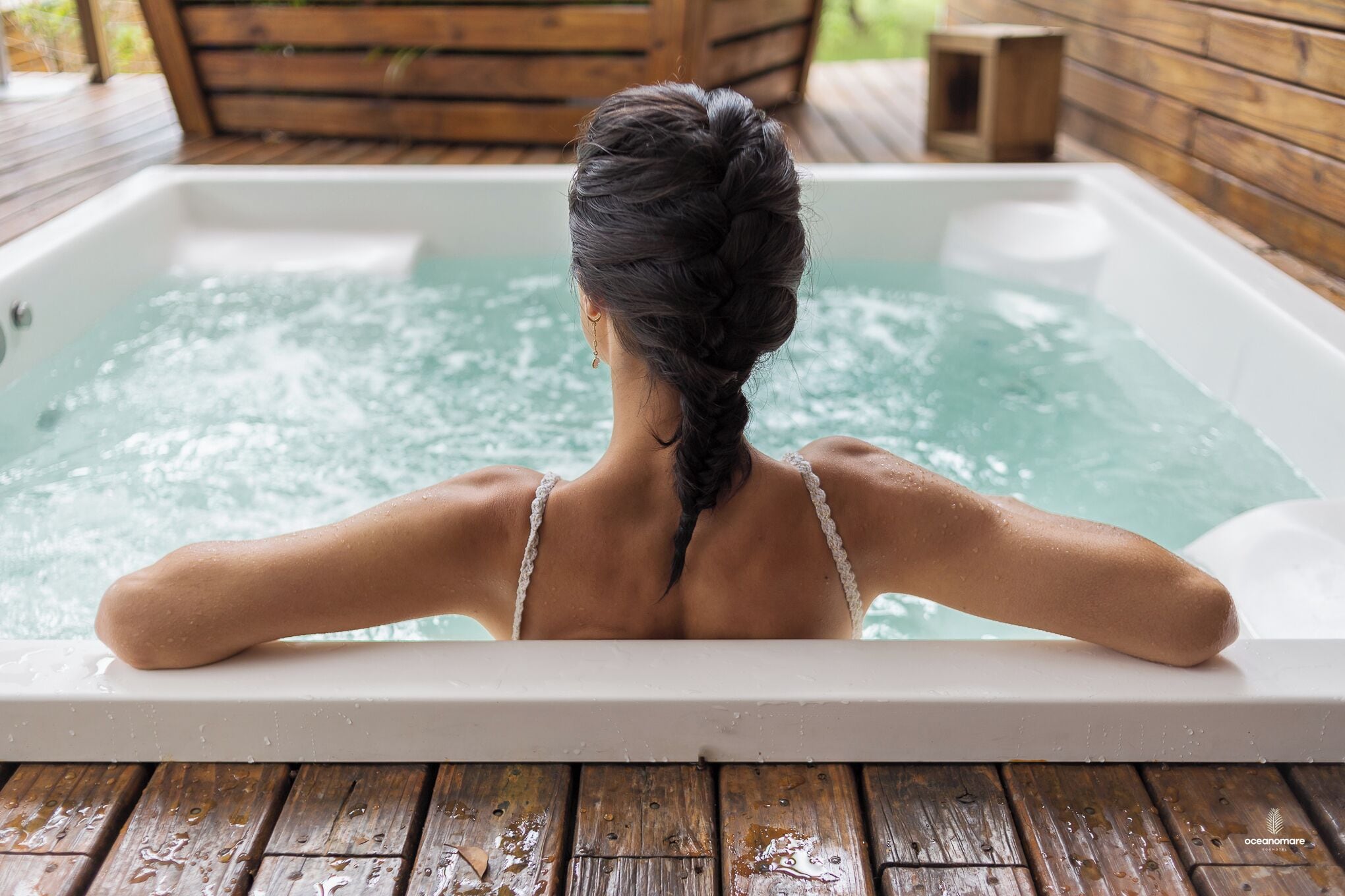 A person relaxing in a hot tub with a wooden deck and wooden walls.