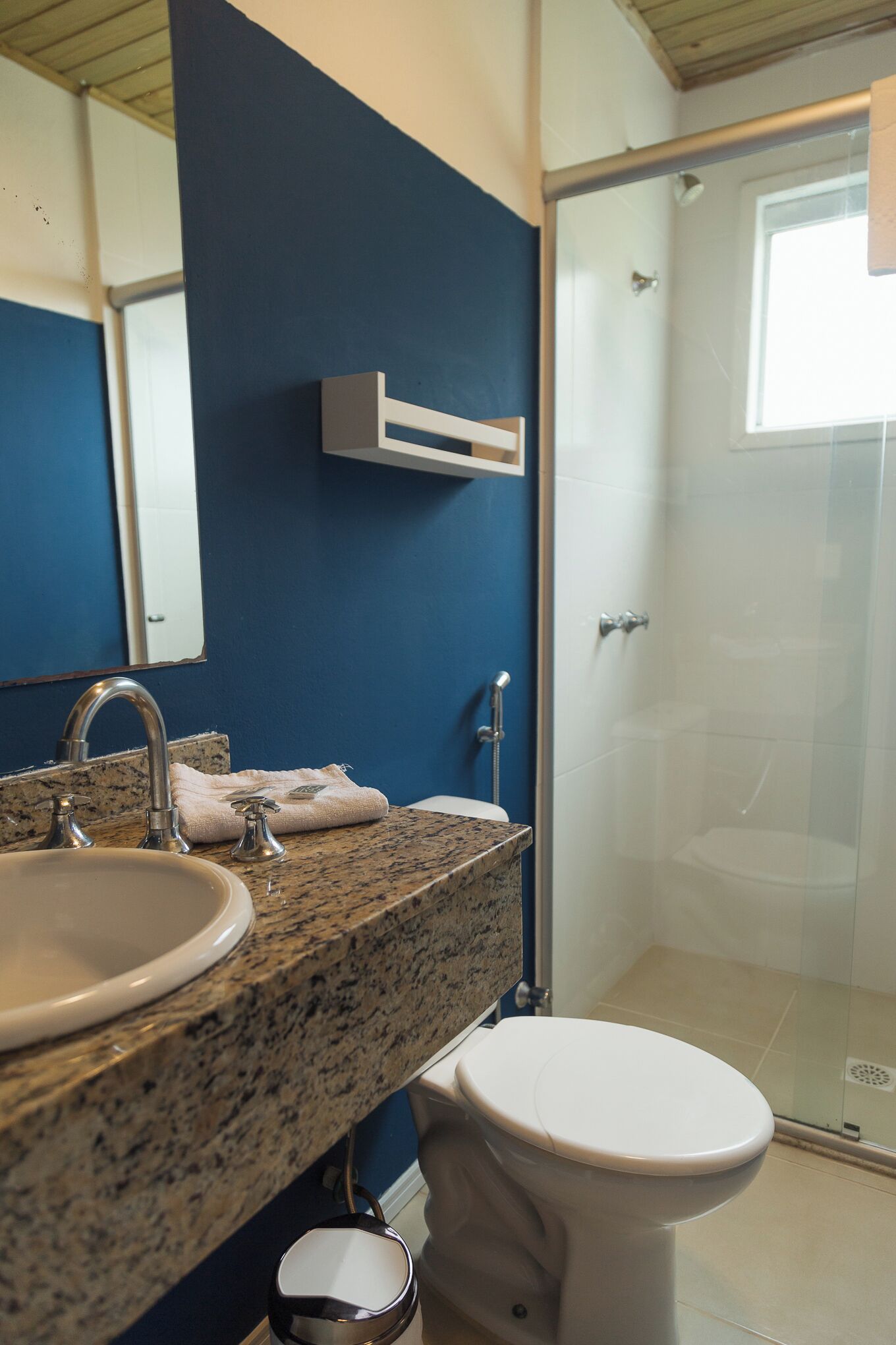 Ein Badezimmer mit Granitplatte, Waschbecken, Toilette und einer Duschkabine aus Glas.