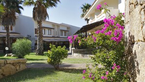 A courtyard with palm trees, a stone wall, and a building with a balcony. - Club Esse Posada Beach Resort (Palau)