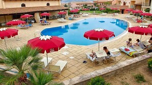 A swimming pool area with red umbrellas, lounge chairs, and a tiled deck. - Club Esse Posada Beach Resort (Palau)