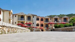 A courtyard with stone walls, red umbrellas, and buildings with balconies. - Club Esse Posada Beach Resort (Palau)