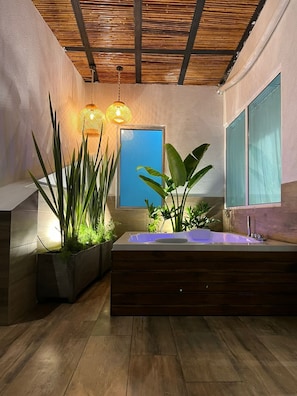 A modern bathroom with a wooden floor, a large bathtub, and potted plants.