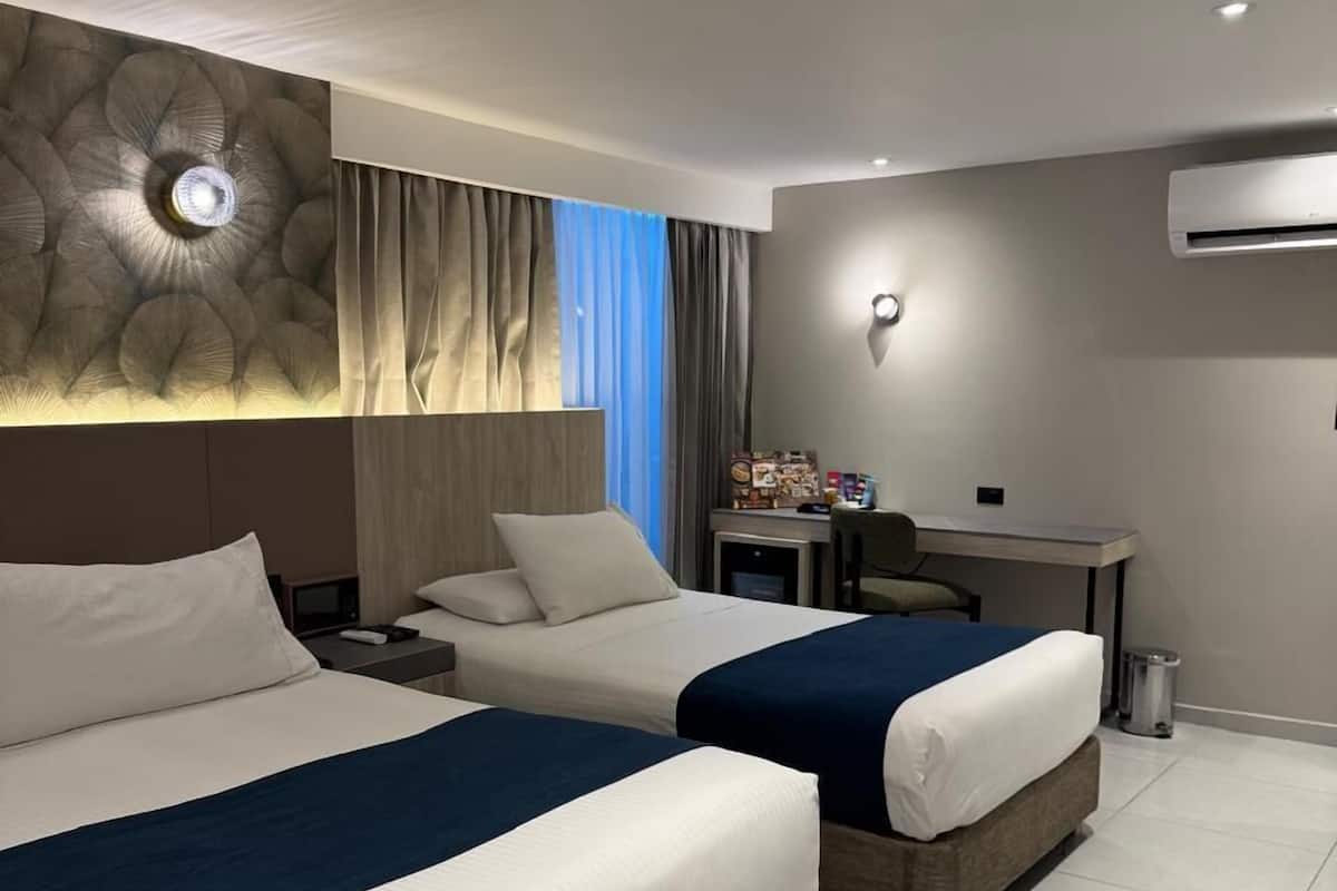 Une chambre d’hôtel avec deux lits, un bureau et un appareil de climatisation.