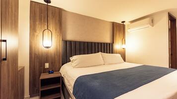 A modern hotel room with a large bed, wooden panel walls, a nightstand, and a wall-mounted air conditioner.