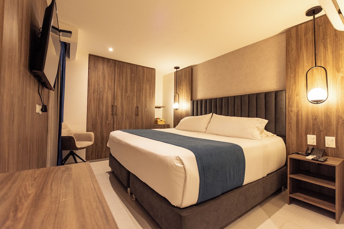 Une chambre d’hôtel moderne, dotée d’un grand lit, d’un bureau, d’une chaise et d’un téléviseur fixé au mur.