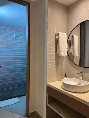 A modern bathroom with a large mirror, a round sink, and a shower area with a glass door.