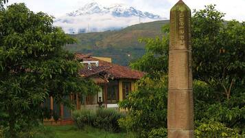 A house with a tiled roof, surrounded by lush greenery and a mountain in the background.