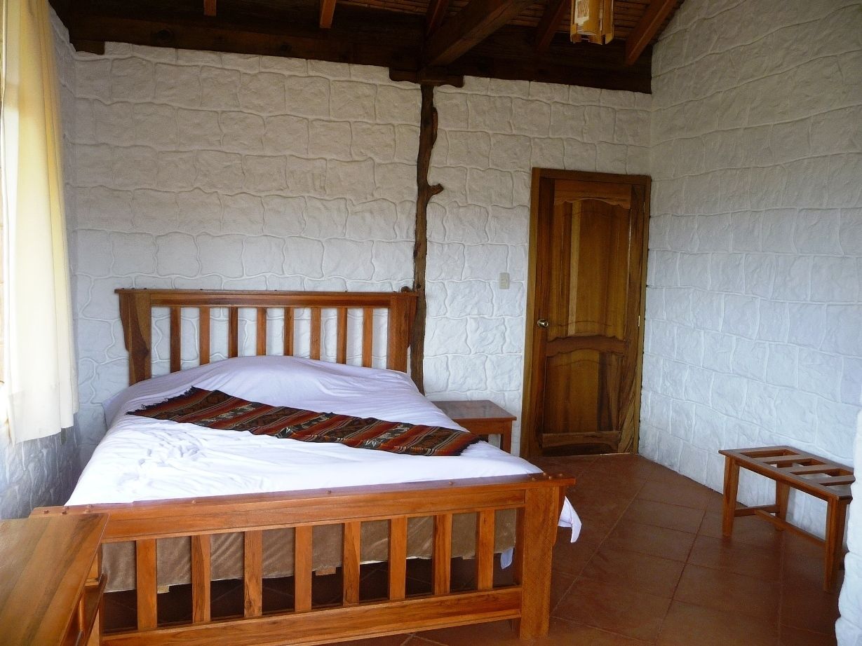 A bedroom with a wooden bed, white walls, and a wooden door.