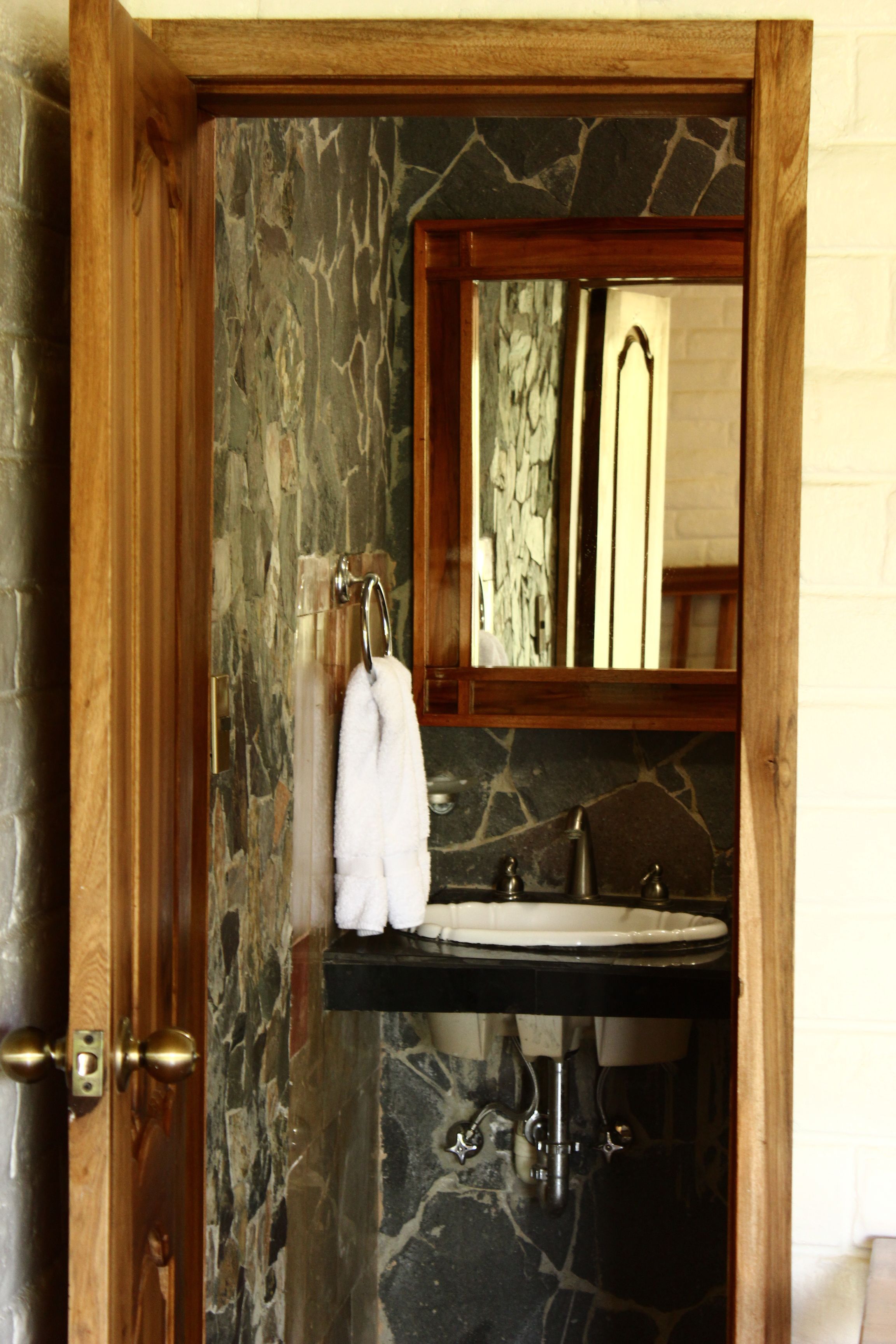 Un baño con pared de piedra, puerta de madera, lavamanos y espejo.