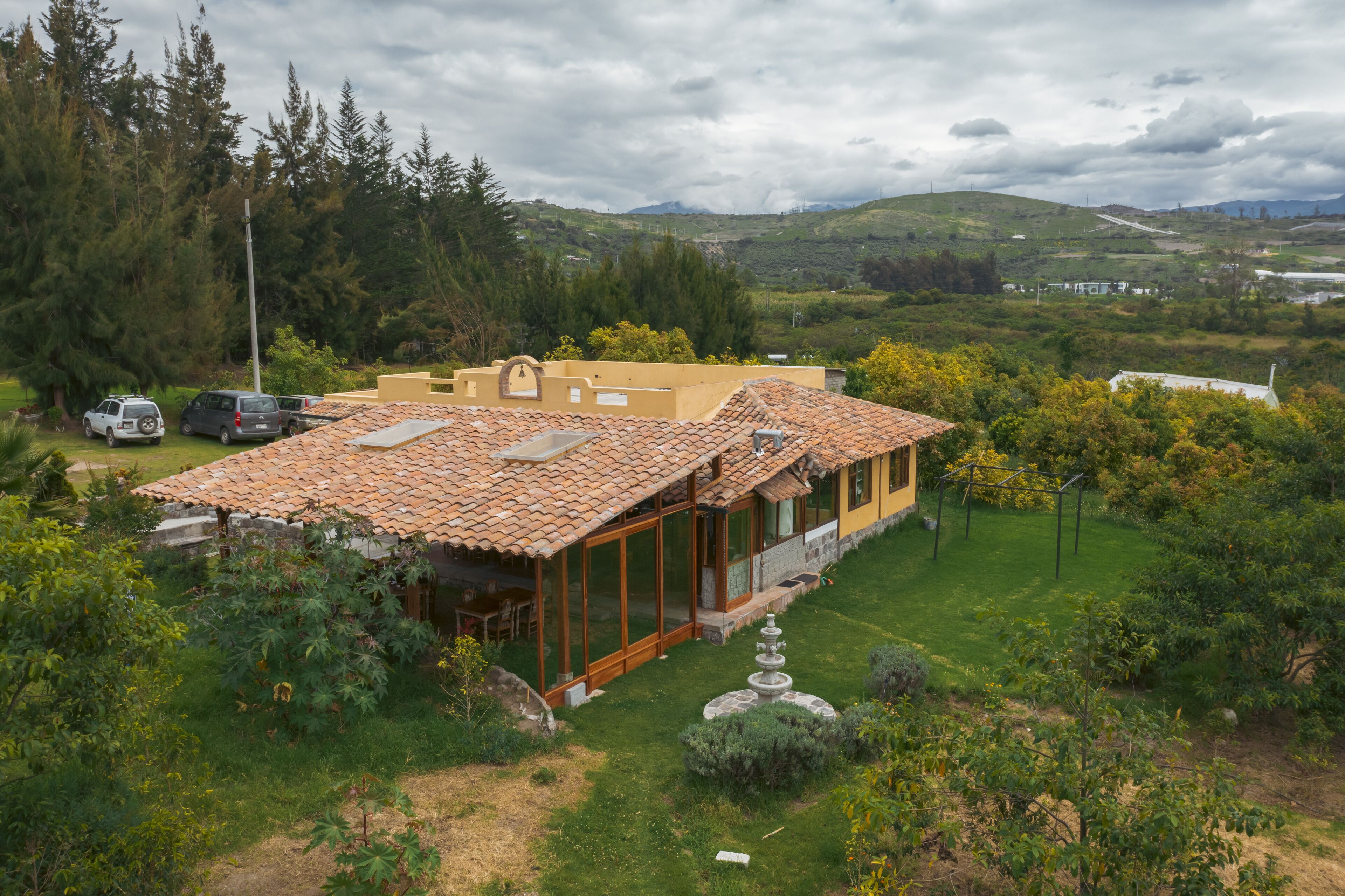 A house with a tiled roof, large windows, and a garden with a fountain.