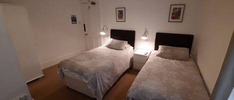 A twin bedroom with two beds, bedside tables, wall-mounted lamps, and framed artwork.