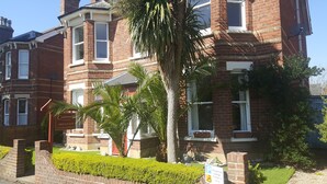 A red brick building with a traditional design, featuring multiple windows and a well-maintained garden with hedges and a palm tree. - Colebrook Guest House (Farnborough)