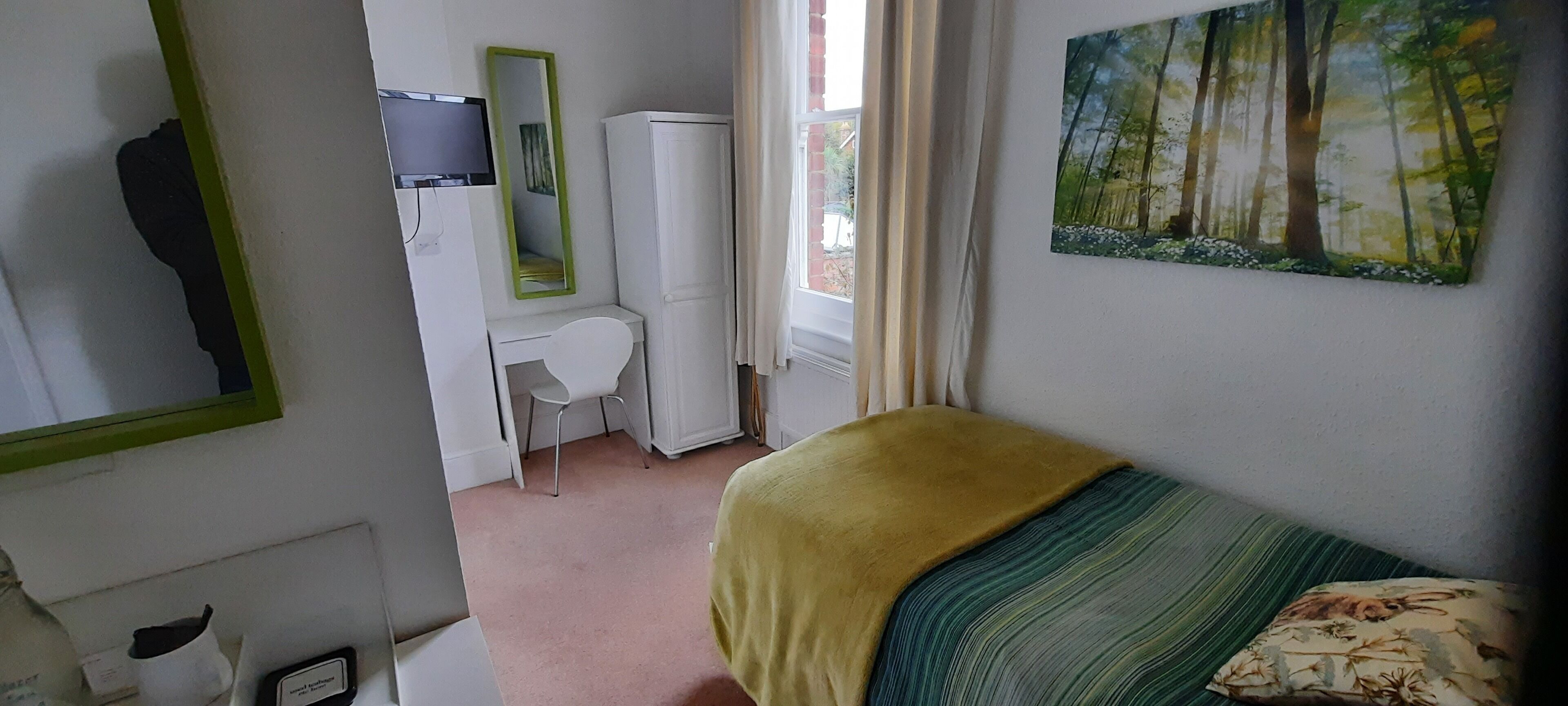 A bedroom with a bed, a desk, a chair, a wardrobe, a mirror, and a painting on the wall.
