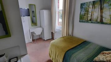 A bedroom with a bed, a desk, a chair, a wardrobe, a mirror, and a painting on the wall.