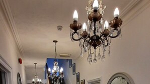 A hallway with wooden flooring, a staircase, a chandelier, a mirror, and a small table with a lamp. - Colebrook Guest House (Farnborough)