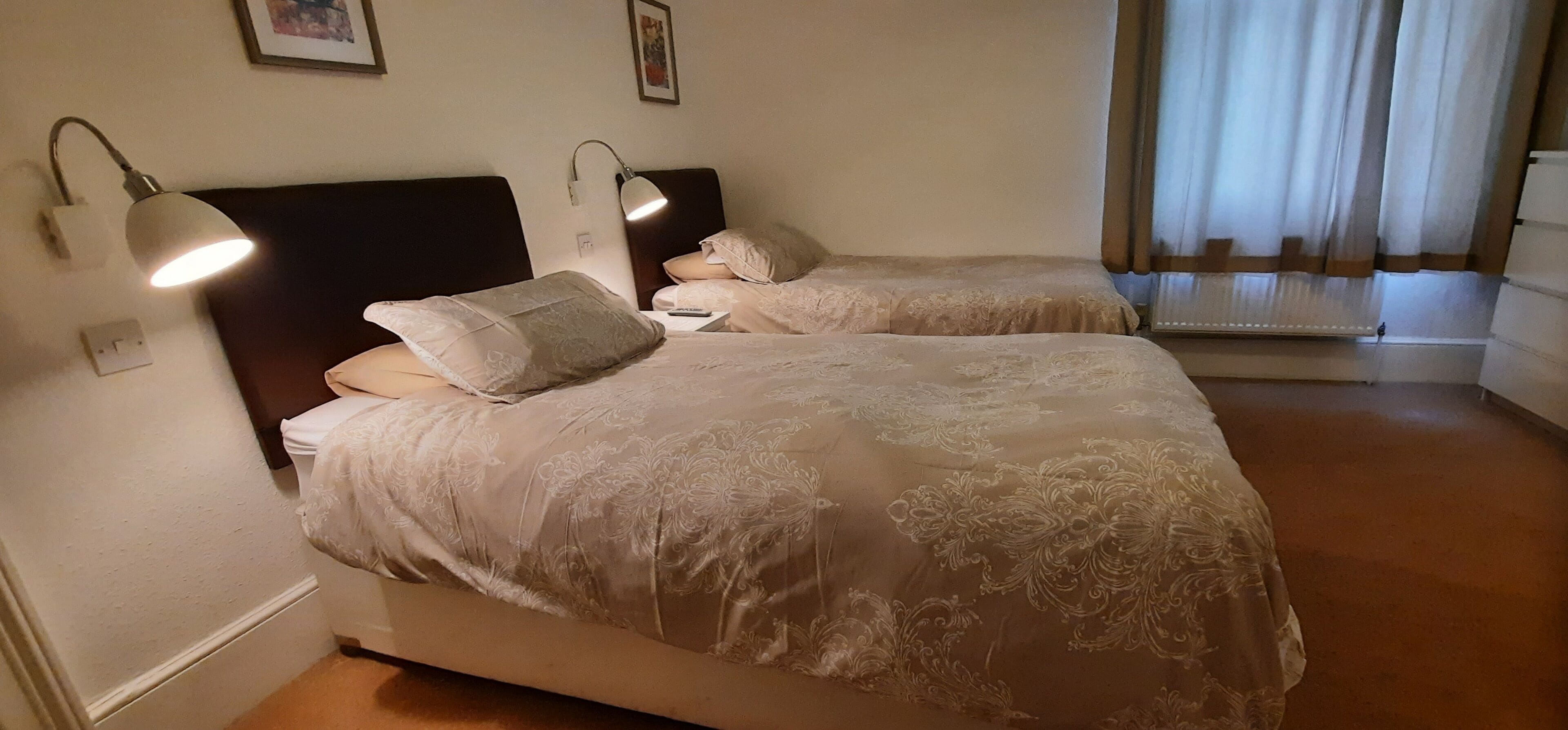 Une chambre d’hôtel avec deux lits, chacun doté d’une tête de lit, de lampes de chevet et d’une couvre-lit à motifs floraux.