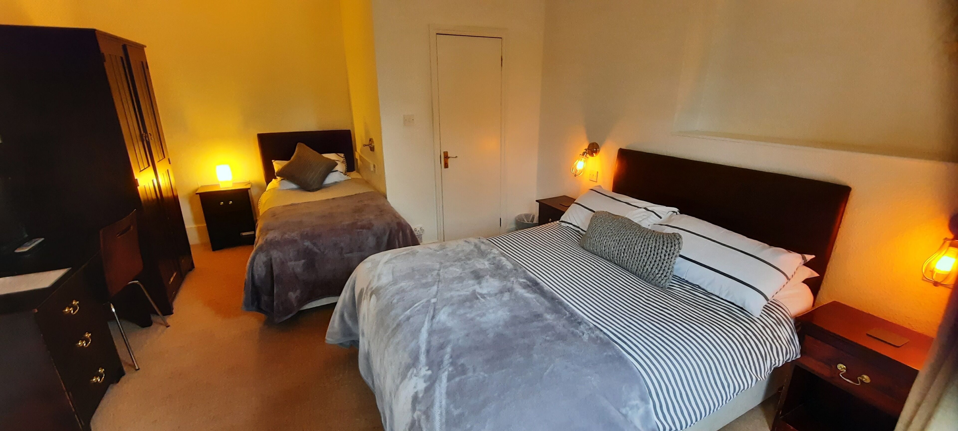 A bedroom with two beds, a wardrobe, and bedside lamps.