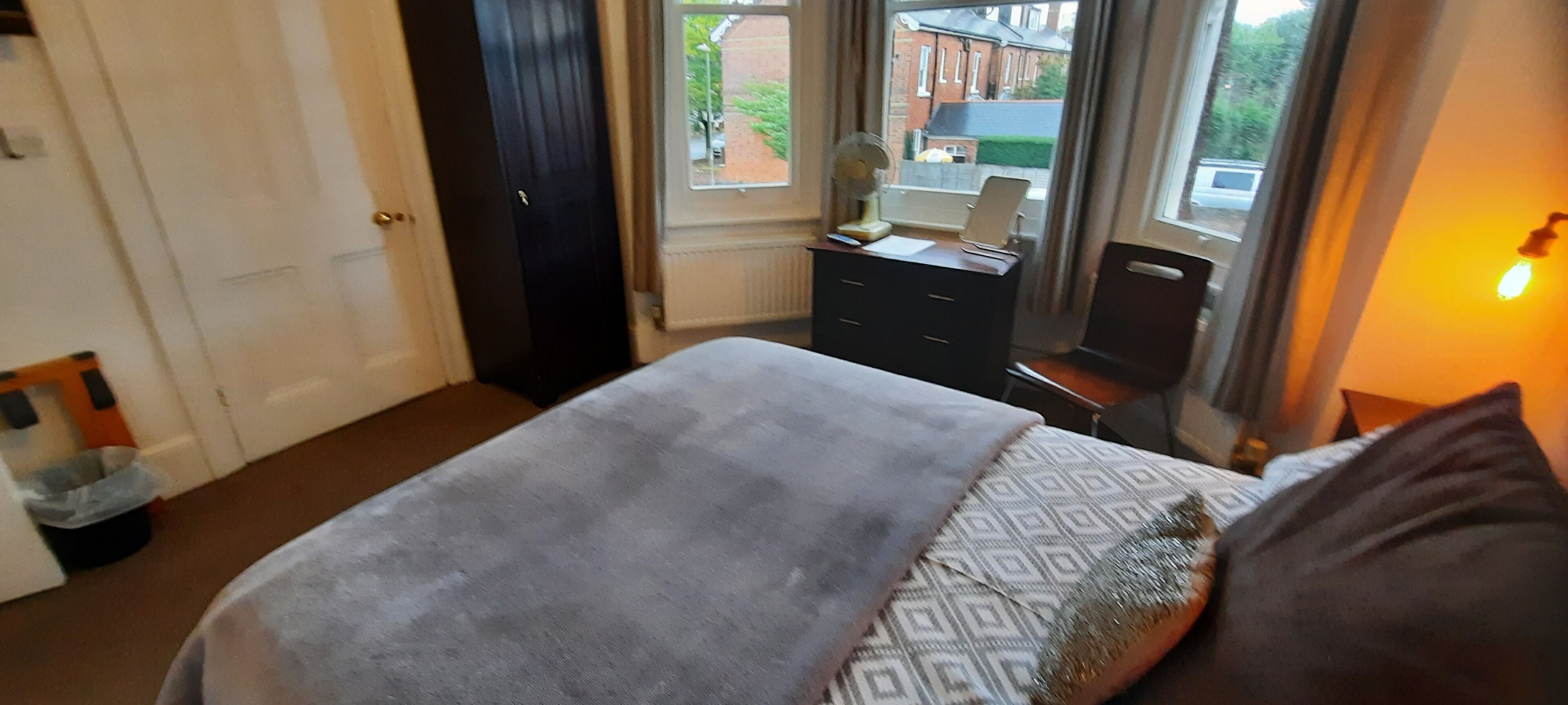 Une chambre à coucher comprenant un lit, une commode, un bureau avec un ordinateur et une fenêtre donnant sur les bâtiments environnants.