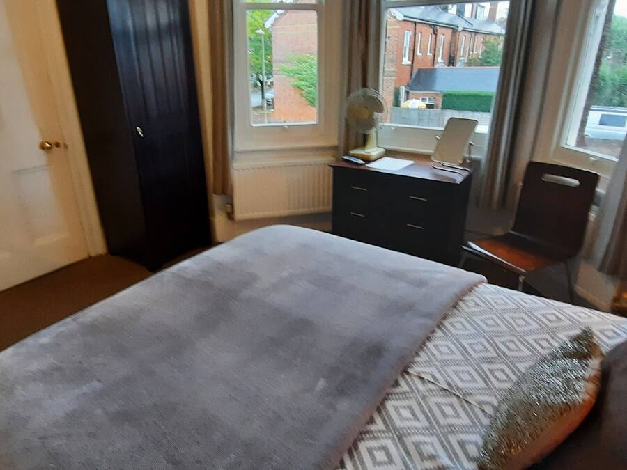 Une chambre à coucher comprenant un lit, une commode, un bureau avec un ordinateur et une fenêtre donnant sur les bâtiments environnants.