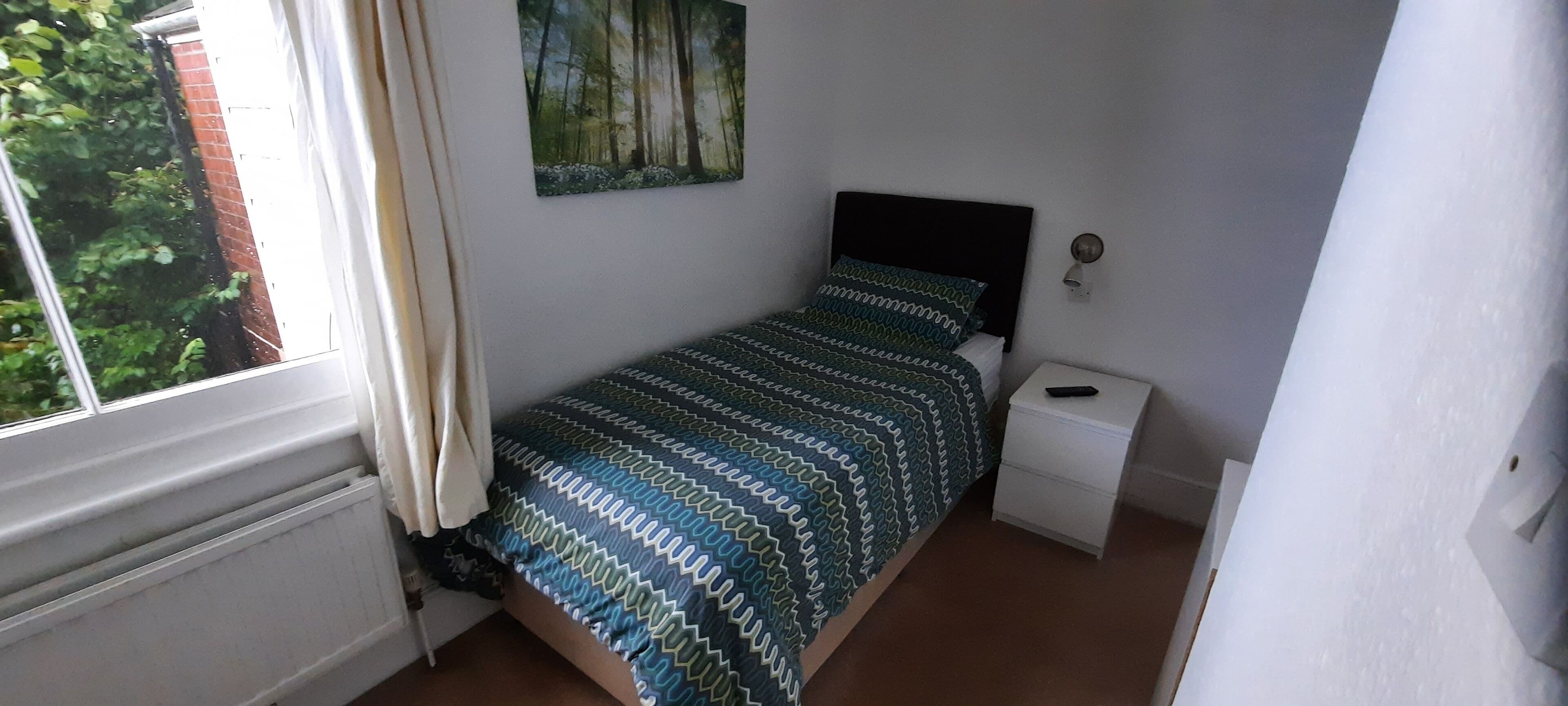 Una camera da letto con un letto, un comodino, una lampada a parete e una finestra con tende.