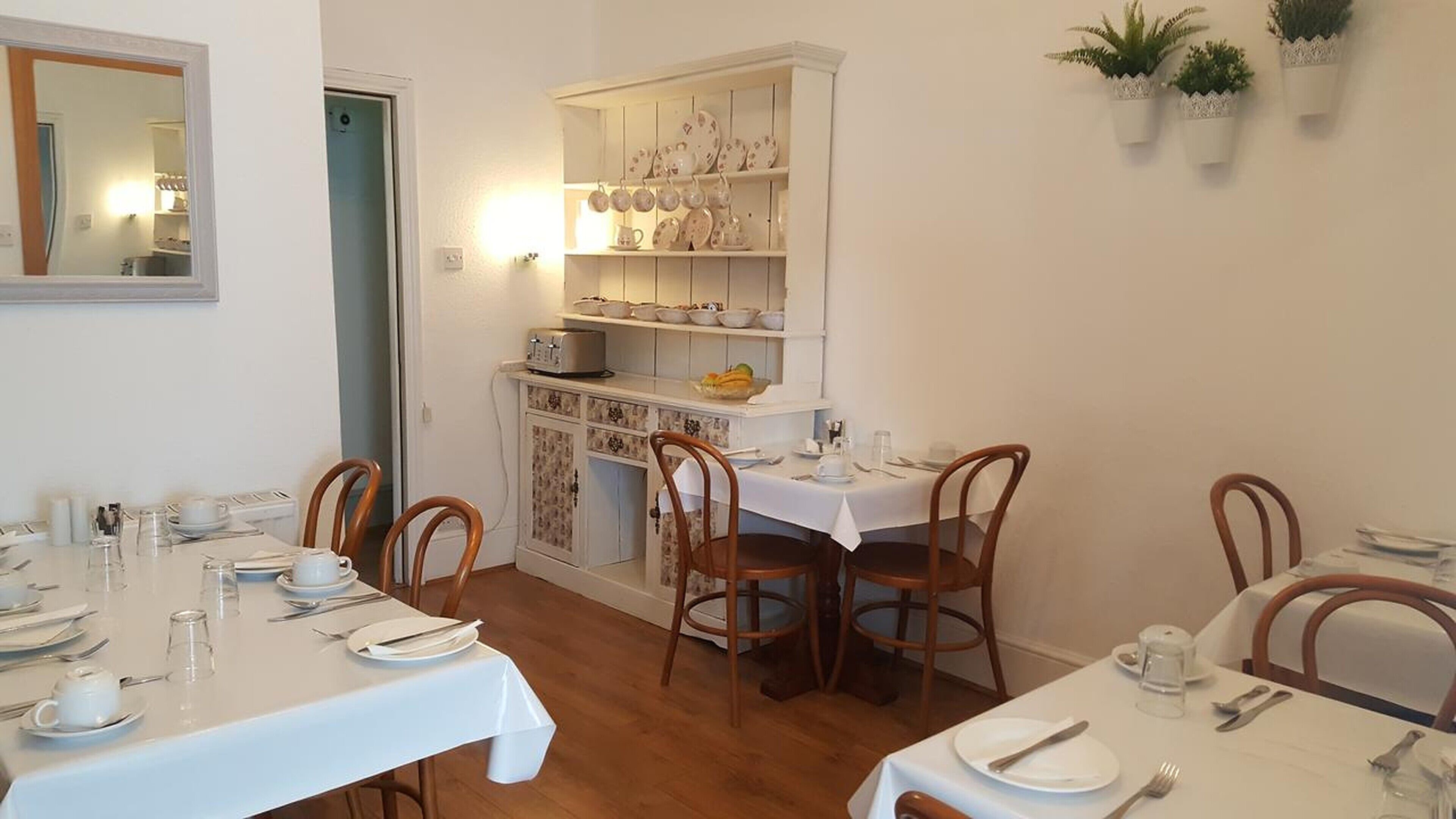 Un espace repas avec des tables et des chaises blanches, ainsi qu’un buffet blanc contenant de la vaisselle.