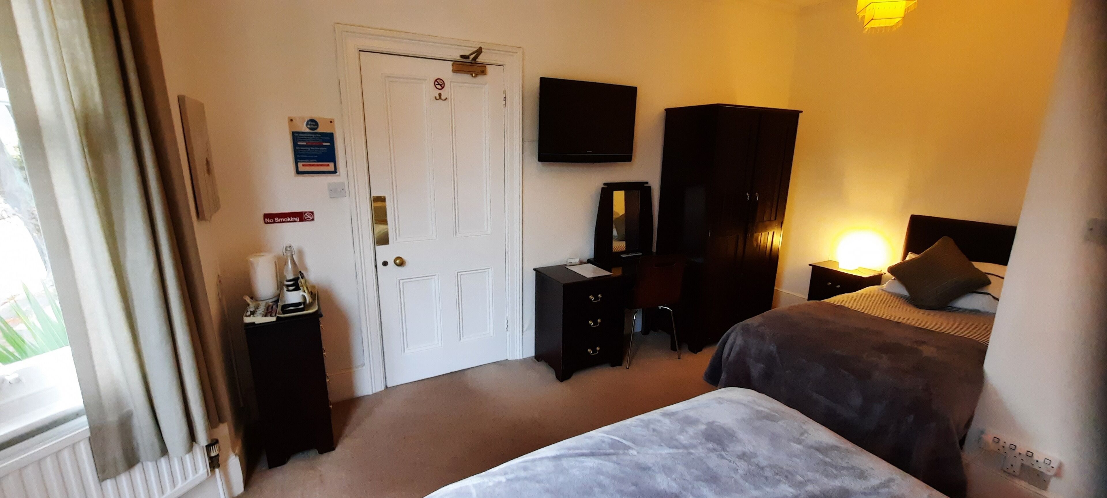 Una camera d'albergo con un letto, una scrivania, un armadio, una televisione e una finestra con tende.
