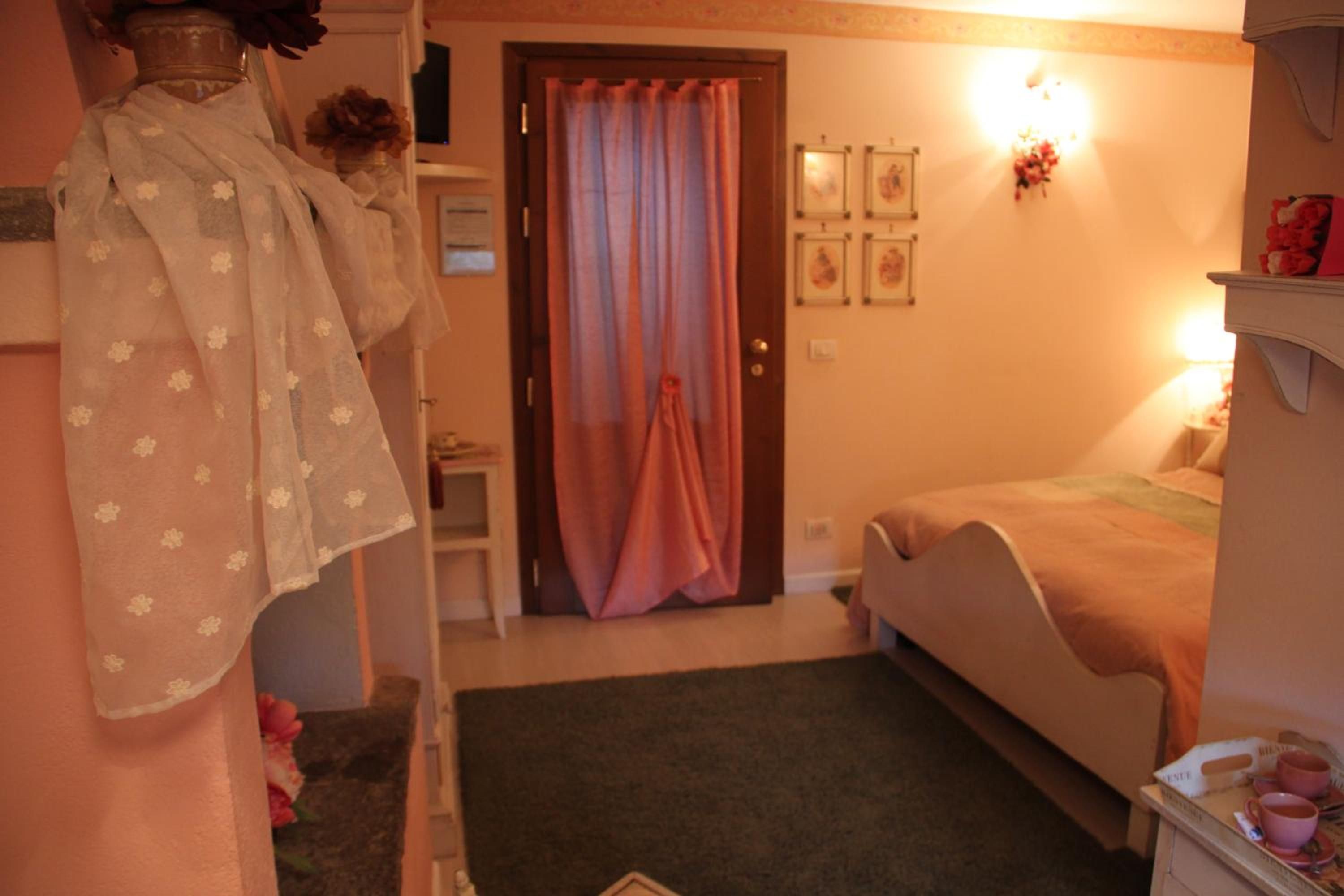 A bedroom with a bed, a bedside table, a dresser, a mirror, a door with curtains, and wall-mounted lights.