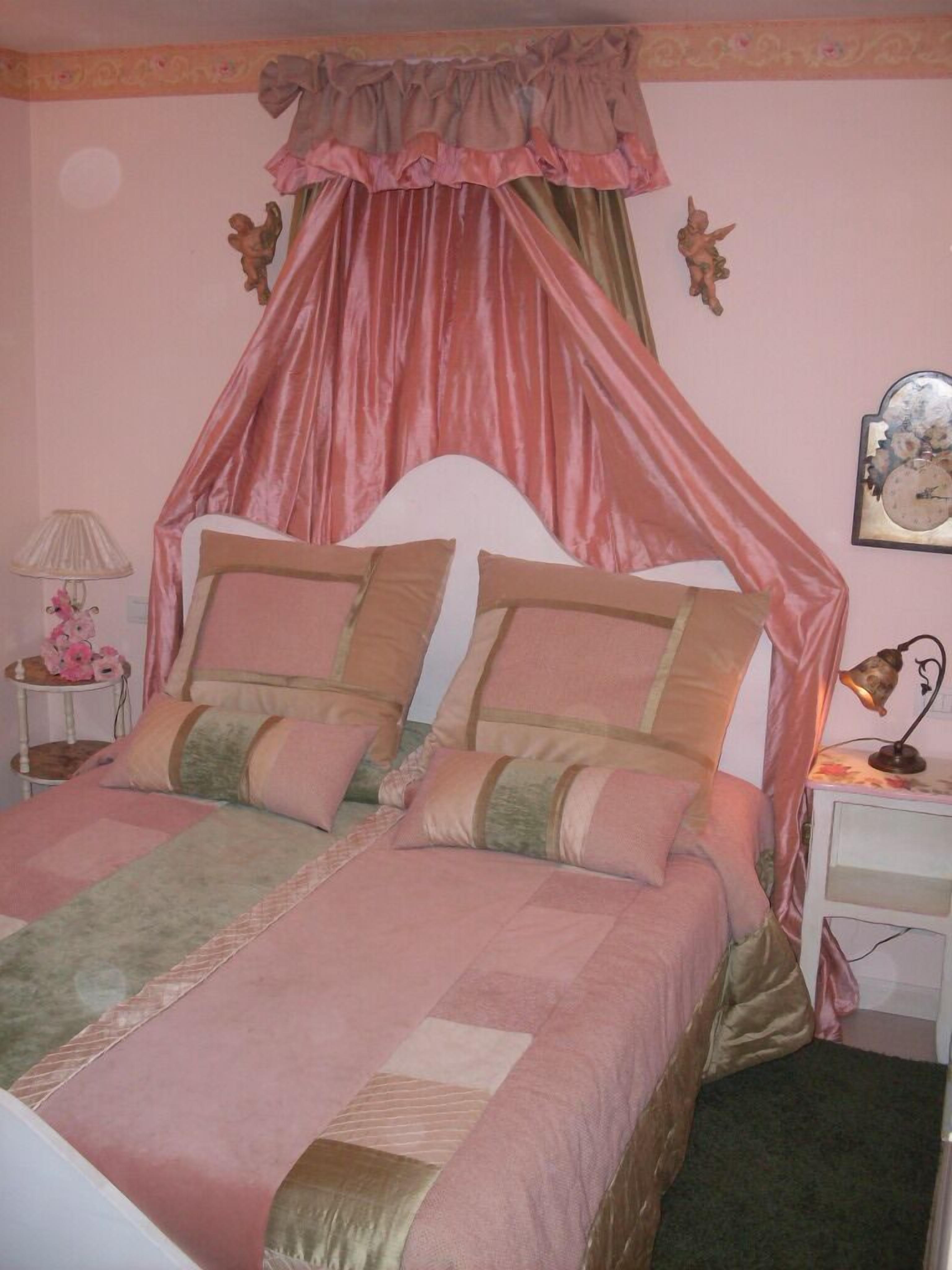 A bedroom with a canopy bed, two bedside tables, a lamp, and a clock on the wall.