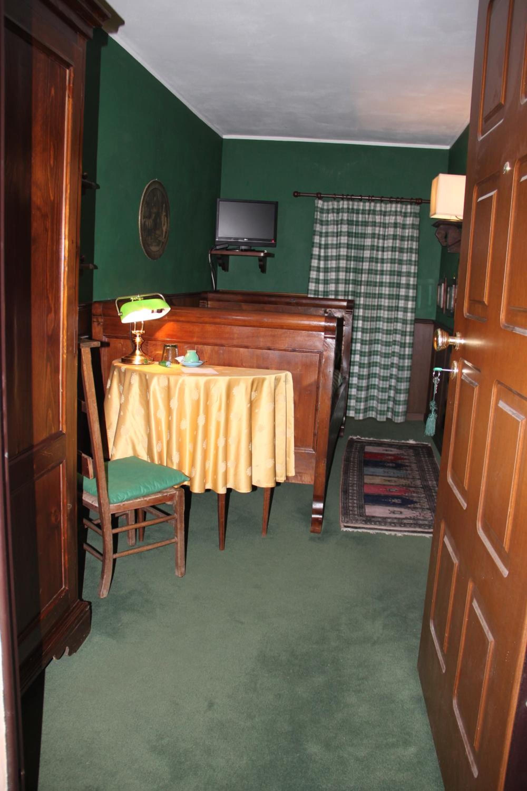 Una stanza con una parete verde, un tavolo di legno con una sedia, un televisore su un mobile, una lampada e una tenda a scacchi.