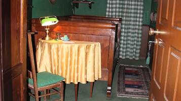 Una stanza con una parete verde, un tavolo di legno con una sedia, un televisore su un mobile, una lampada e una tenda a scacchi.