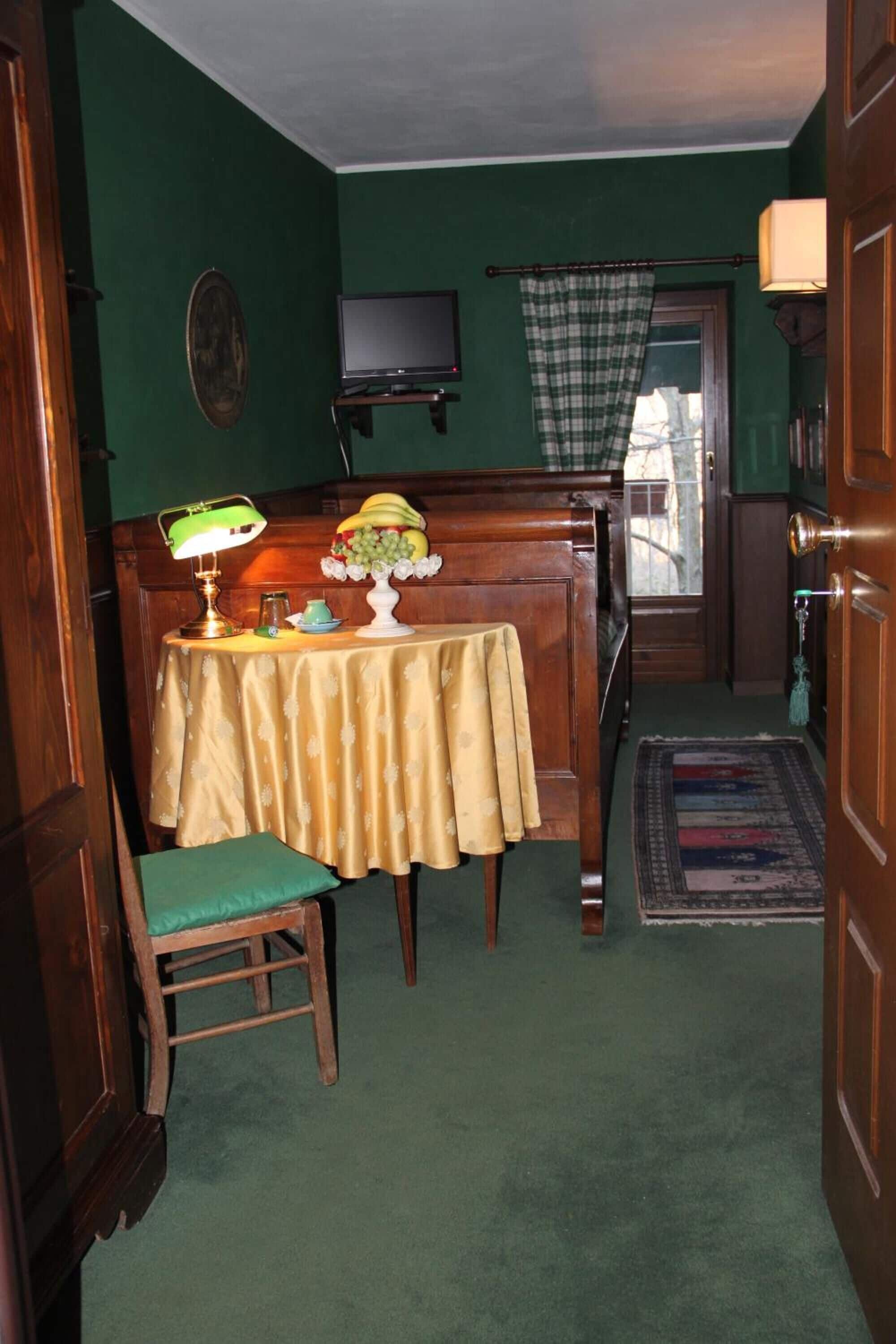Ein Zimmer mit grüner Wand, einer Holzbänkl, einem Tisch mit einer Lampe und einem Fernseher an der Wand.