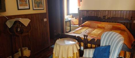 Ein Schlafzimmer mit einem hölzernen Bett, einem Sessel, einem kleinen Tisch und zwei gerahmten Bildern an der Wand.
