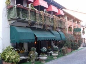 A building with a green awning, potted plants, and a red umbrella. - Affittacamere Una Franca (Biella)