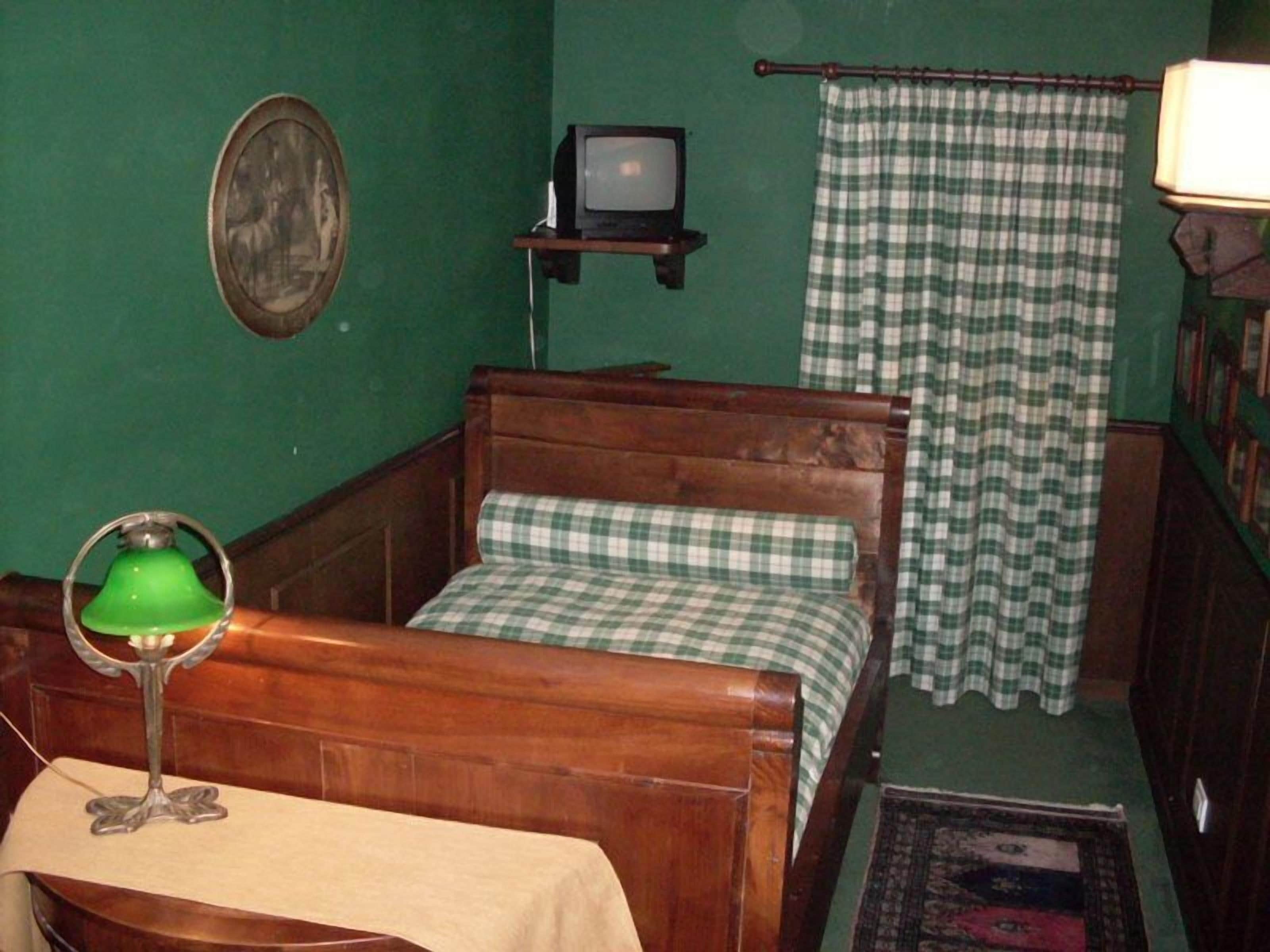 A room with a wooden bed, a green wall, a small television, and a green lamp.
