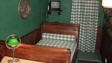 A room with a wooden bed, a green wall, a small television, and a green lamp.