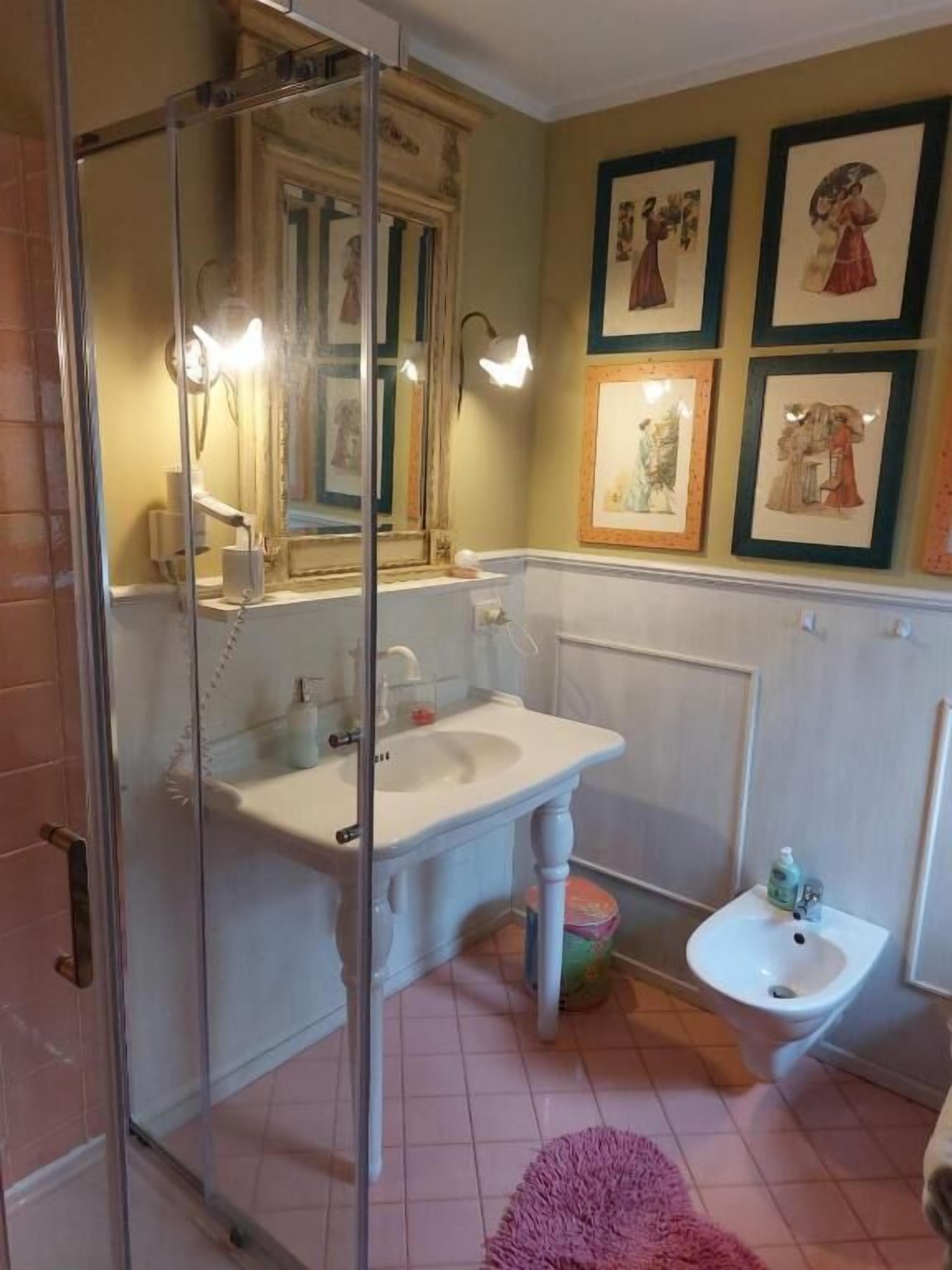 Une salle de bain dotée d’une douche à parois de verre, d’un lavabo, d’un bidet et d’œuvres d’art encadrées accrochées au mur.