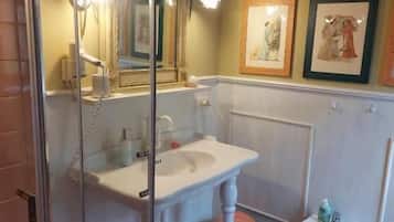 Une salle de bain dotée d’une douche à parois de verre, d’un lavabo, d’un bidet et d’œuvres d’art encadrées accrochées au mur.