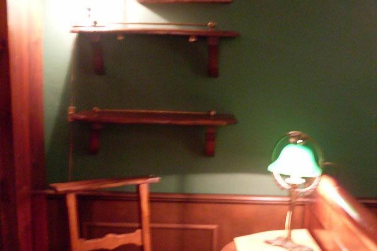 A small, dimly lit room with a single wooden chair, a table with a green cloth, and a wall-mounted shelf.