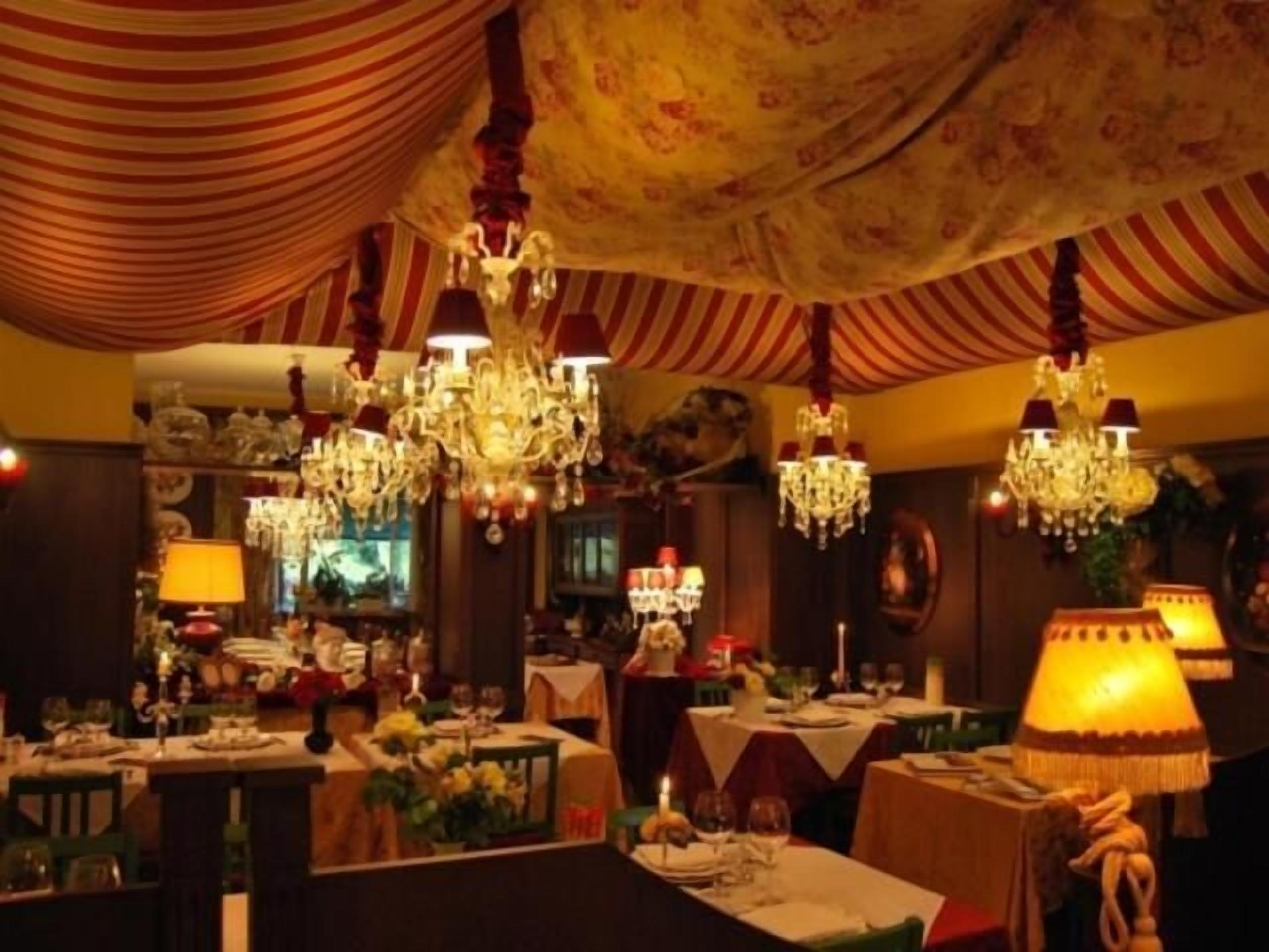 Een eetruimte met meerdere tafels, kroonluchters en stoffen draperingen aan het plafond.