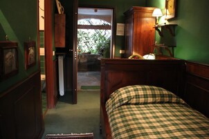 Una habitación con cama de madera, pared verde, aparador de madera y puerta que da a un espacio exterior.