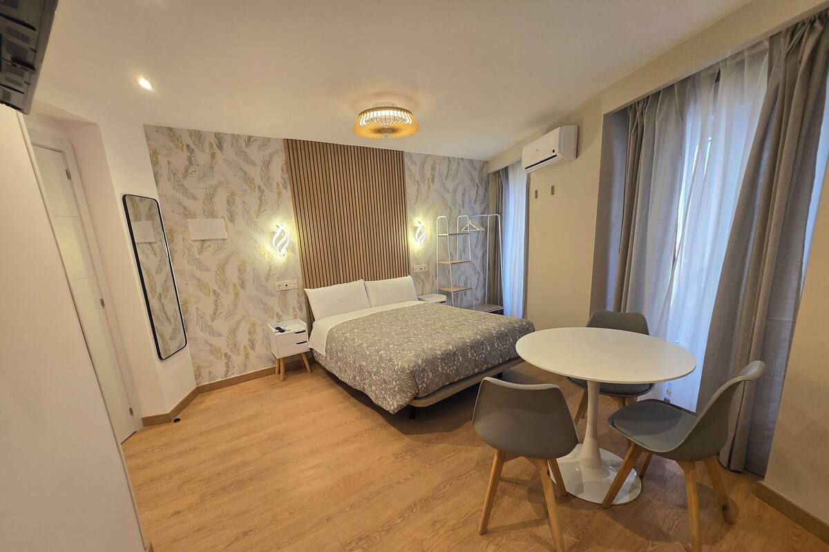 A modern hotel room with a bed, bedside table, chair, and a small round table with two chairs.