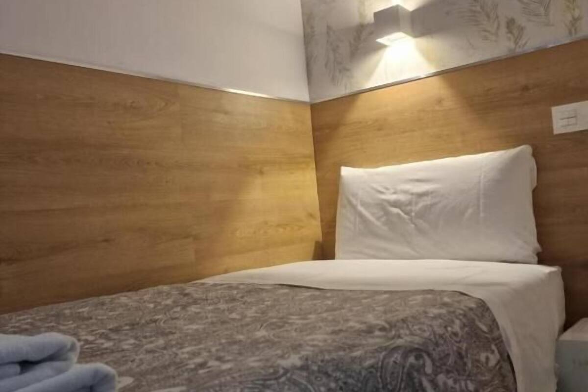A hotel room with a wooden headboard, a patterned bedspread, and a wall-mounted light fixture.