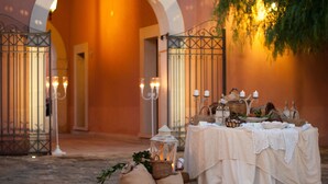 Un espace de restauration en plein air avec une table recouverte d’une nappe blanche, entourée de bougies et d’objets décoratifs.