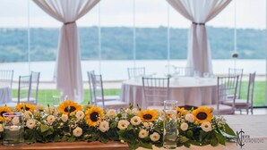 Une table décorée de tournesols et de verres, donnant sur une étendue d’eau.