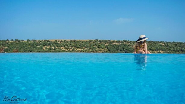 Une personne est assise dans une piscine à l’eau cristalline, avec en arrière-plan une colline boisée.